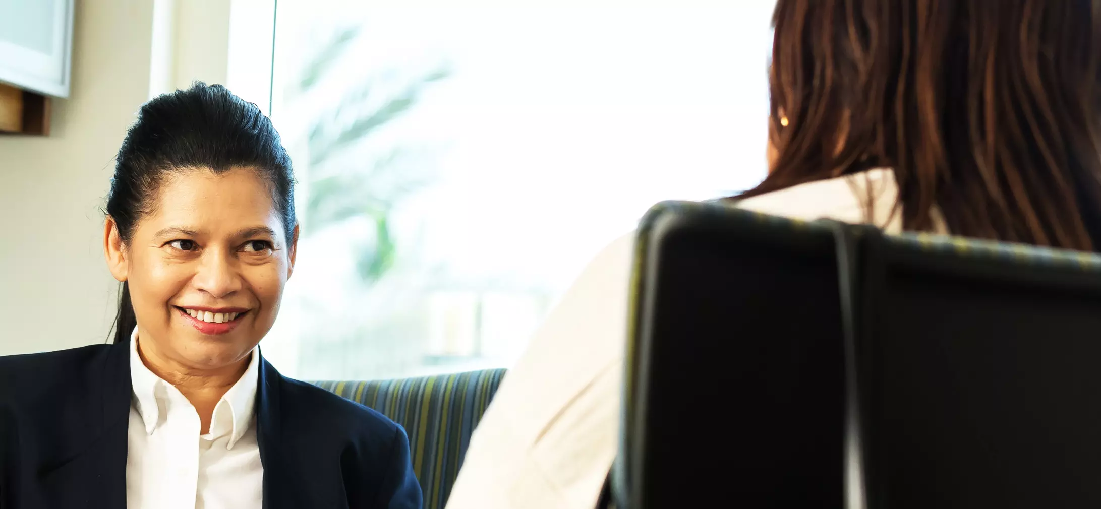 Business professional women behind desk smiling and talking to a person across from her