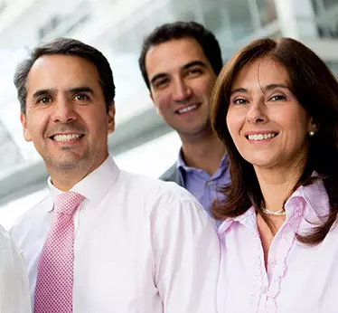 Two men and one women standing together smiling, wearing formal work attire